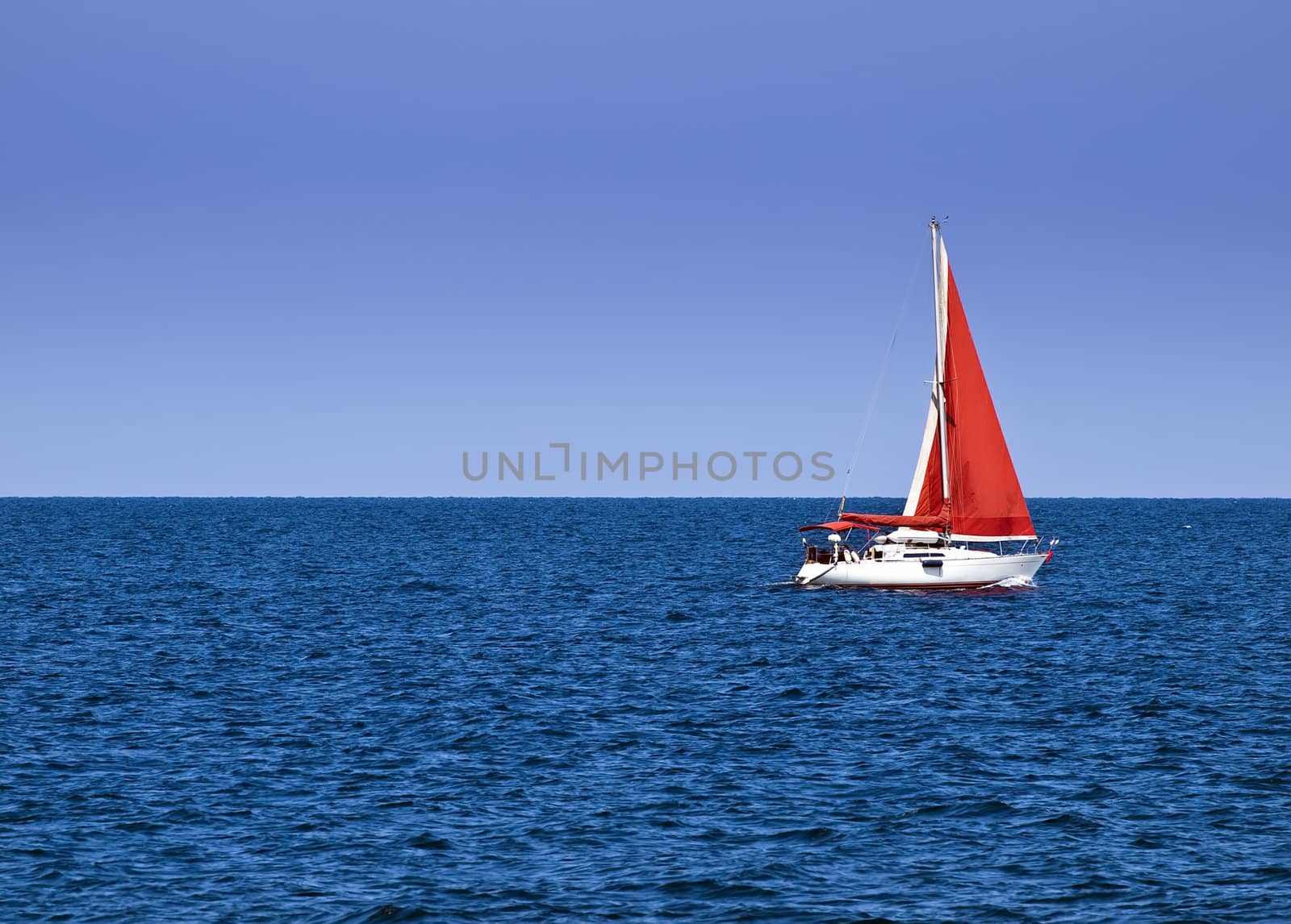 Yacht with a red sail offering crisp contrast against sky and ocean blue