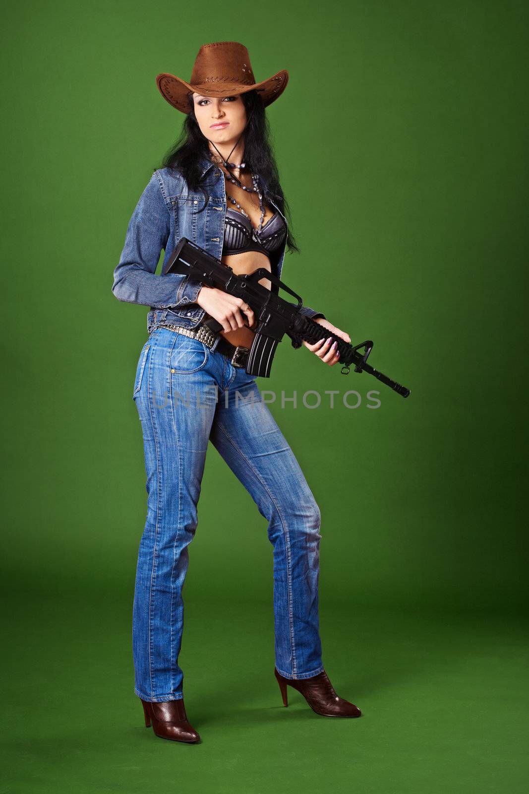 Young beautiful woman in jeans with a rifle on a green background
