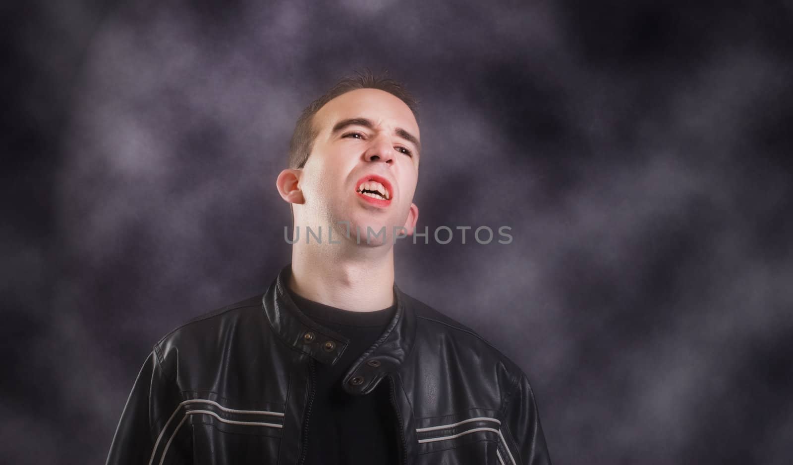 A modern day vampire showing his teeth, while standing in a dark foggy room