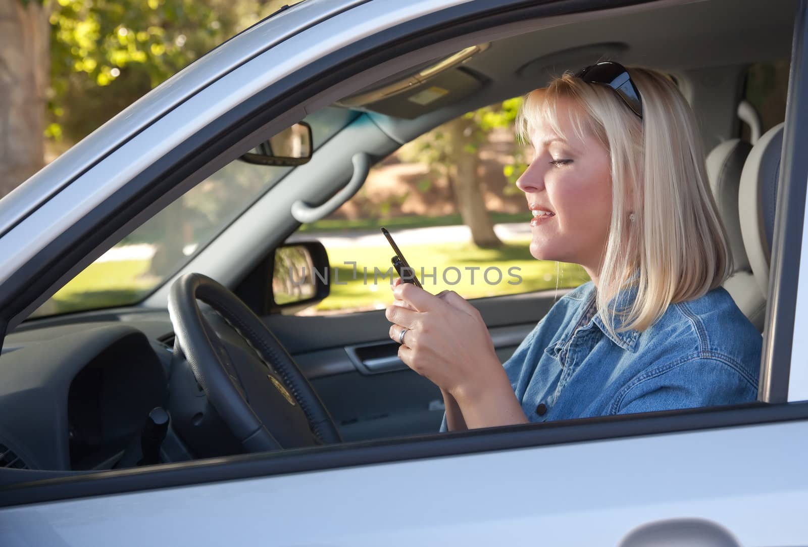 Attractive Blonde Woman Text Messaging on Her Cell Phone While Driving.