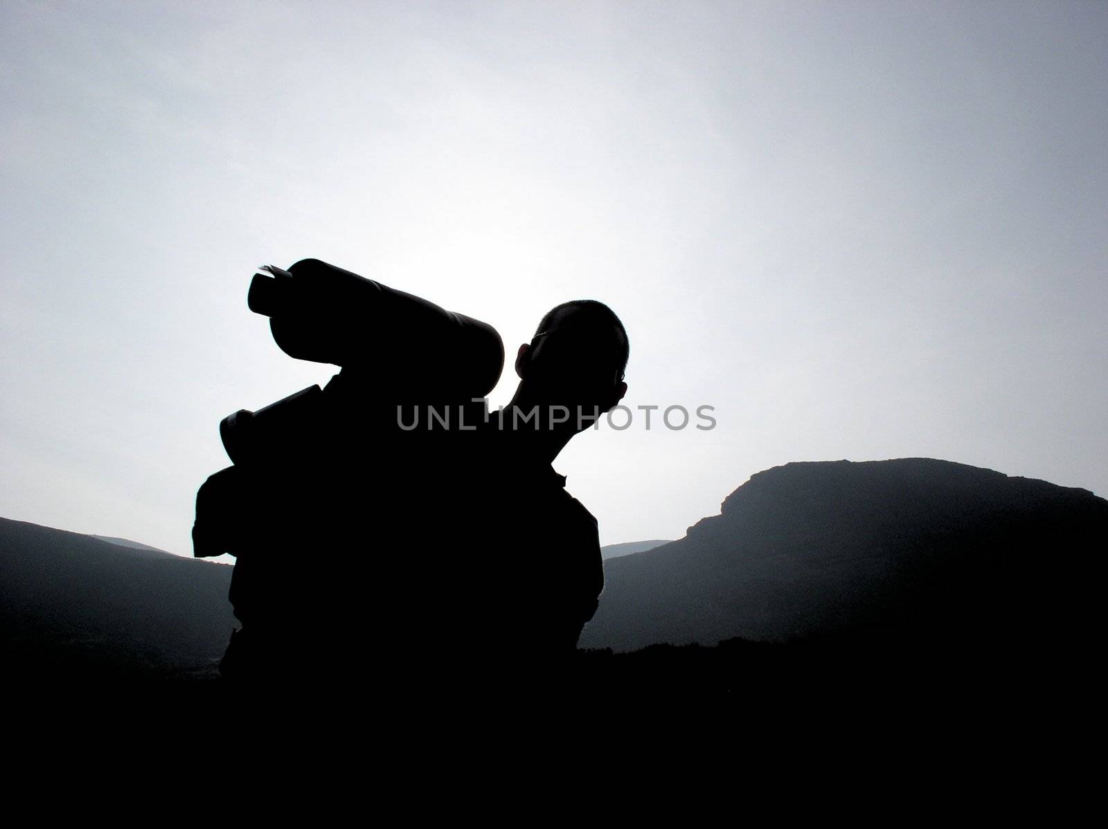 An unidentified hiker stands silhouetted against the sun, with mountains behind.