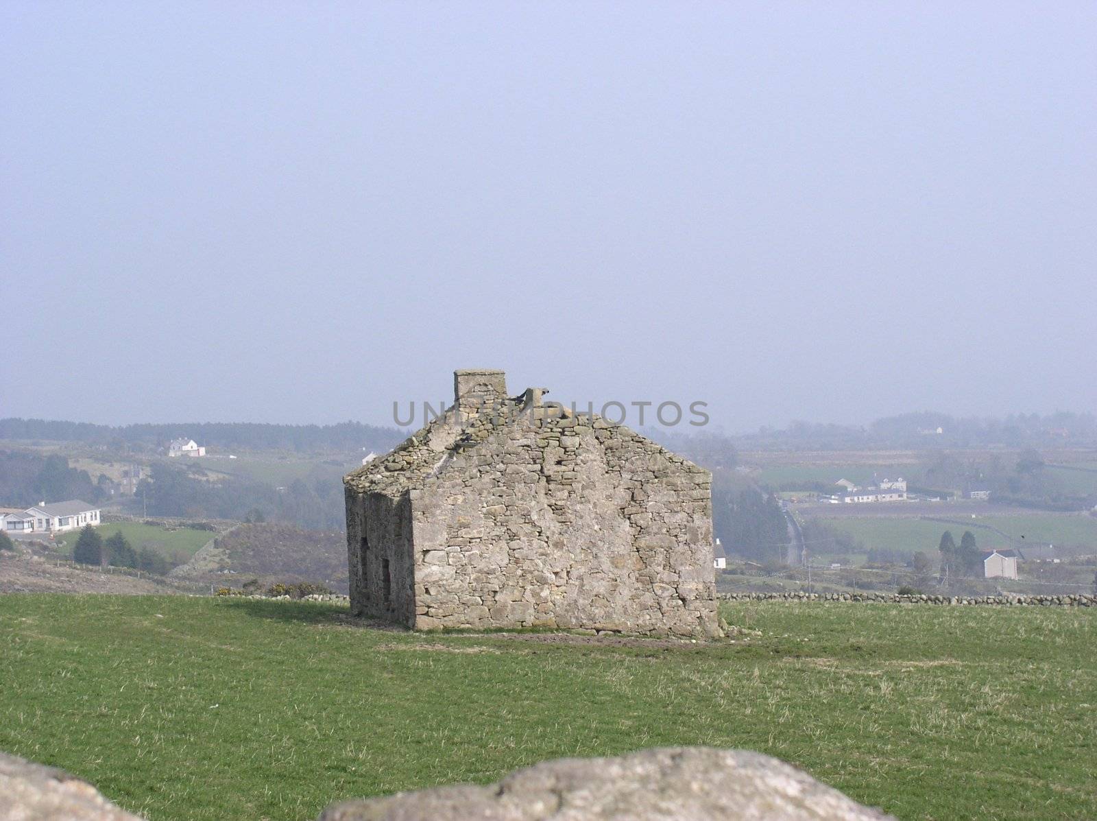 An old stone cottage stands derelict in a field.