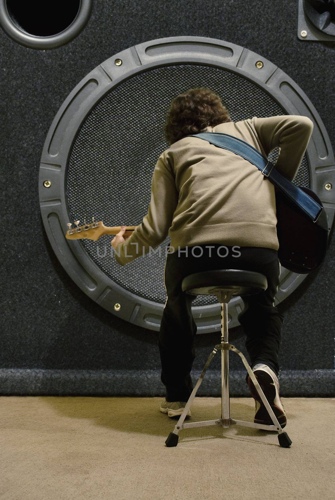 Base guitarist (from behind) playing very close to an impossibly big speaker.