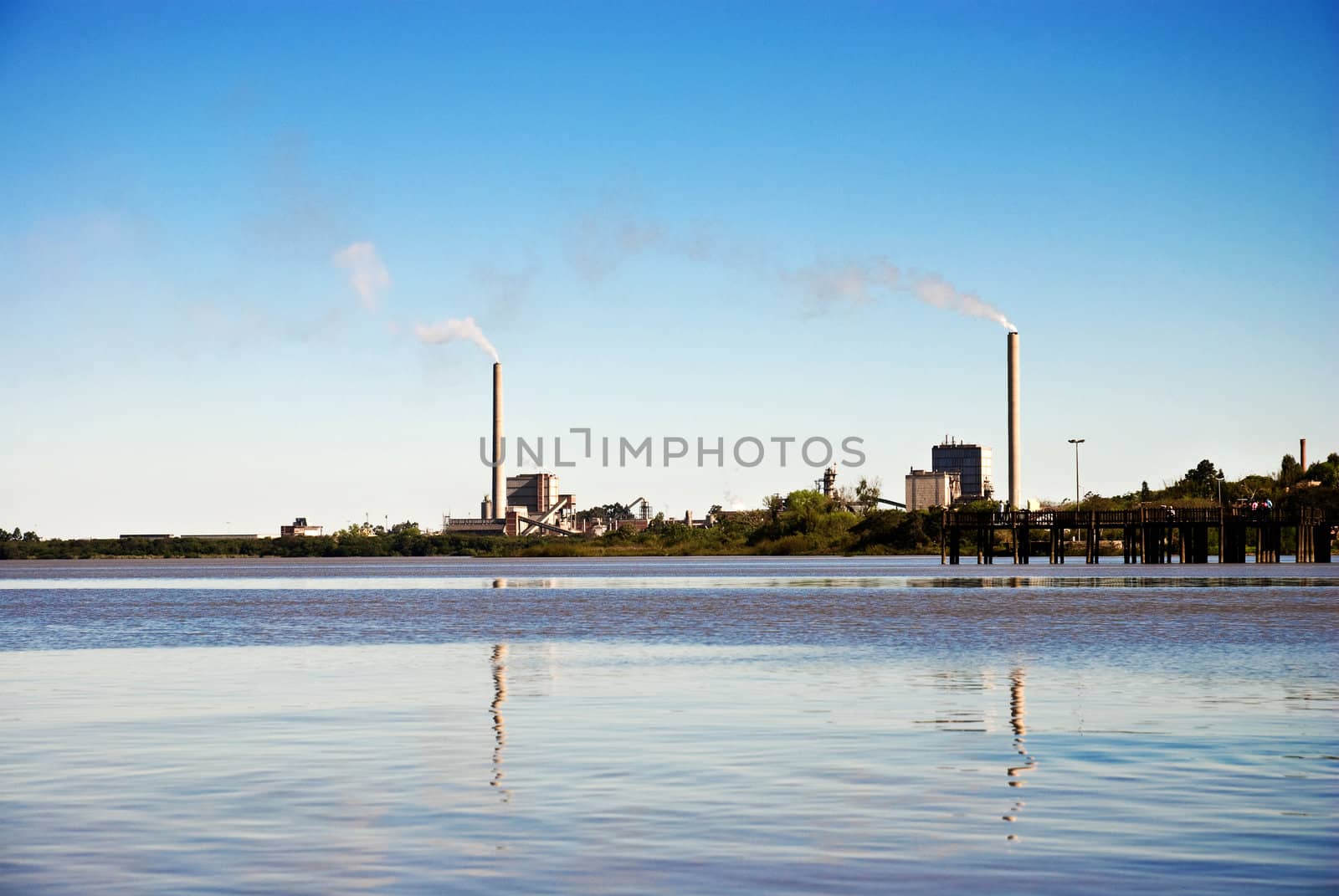 Lake and blue sky with two factory chimneys far away emitting fumes.