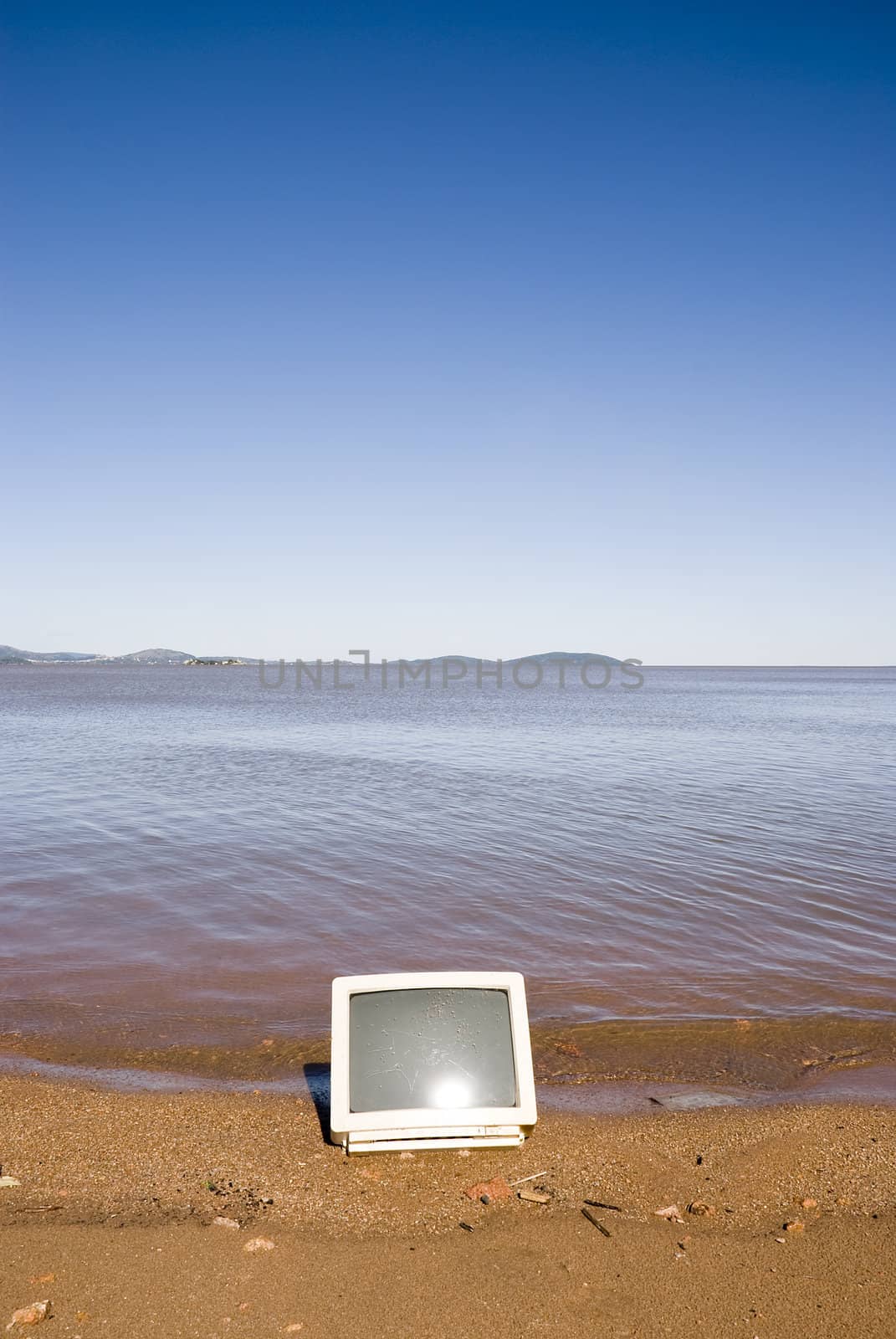 A computer monitor in the sand, with blue sky. Coastline shot.