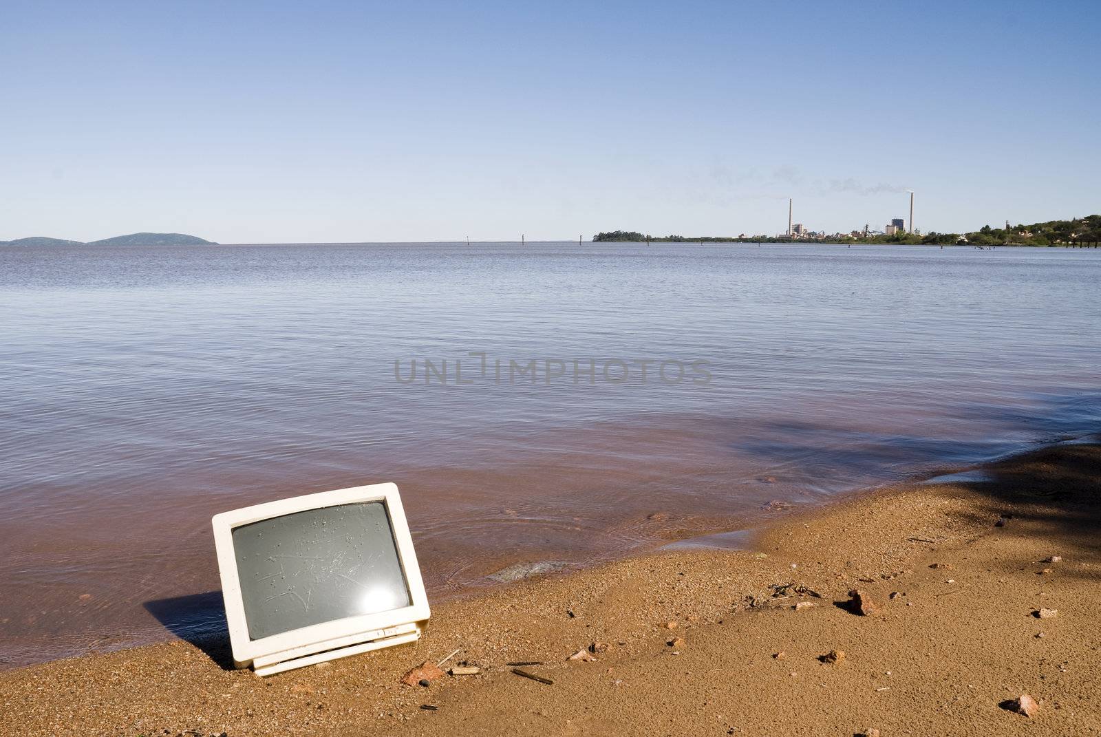 Computer monitor in the sand, with calm lake in the background. With copy space.