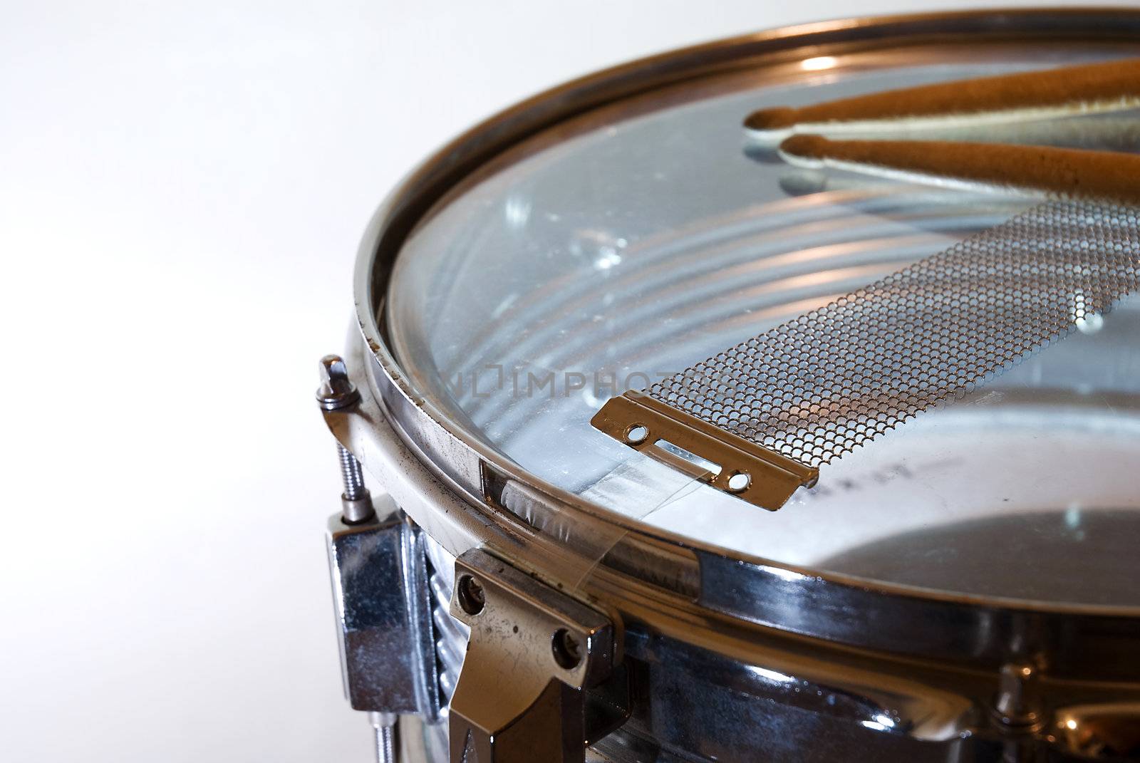 Detail of a snare drum (upside down) with drumsticks resting on it.