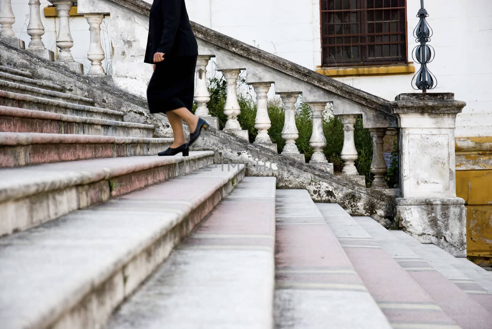 Black dressed female figure climbing up an old staircase. Shot is sideways.