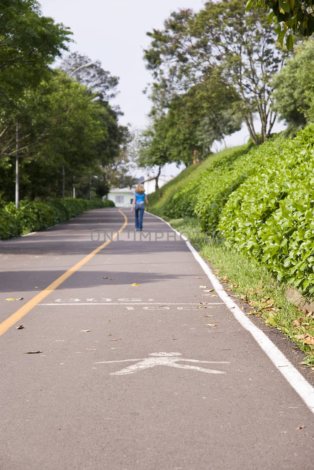 Perspective shot of a road with a pedestrian symbol painted on it and with female figure walking in the background.