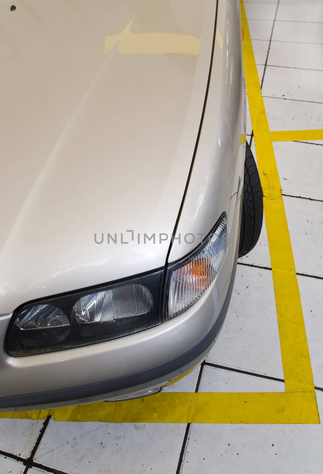 Detail shot of front of a modern beige car with yellow parking lines on the floor. Shot from above.