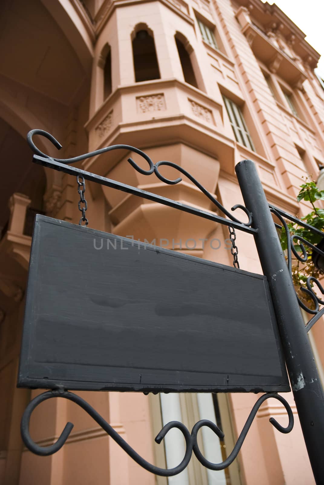 Dark wooden sign board with pink Victorian building in the background. Low angle shot.