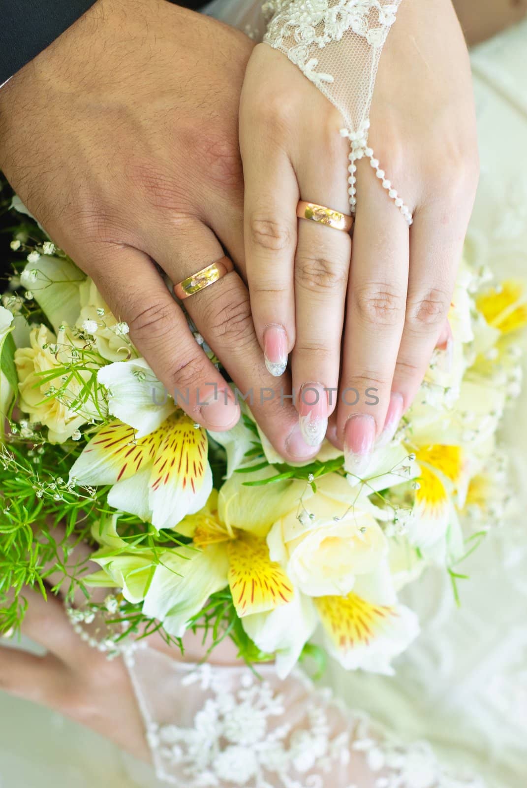 Hands of bride and groom with wedding rings over the bridal bouquet