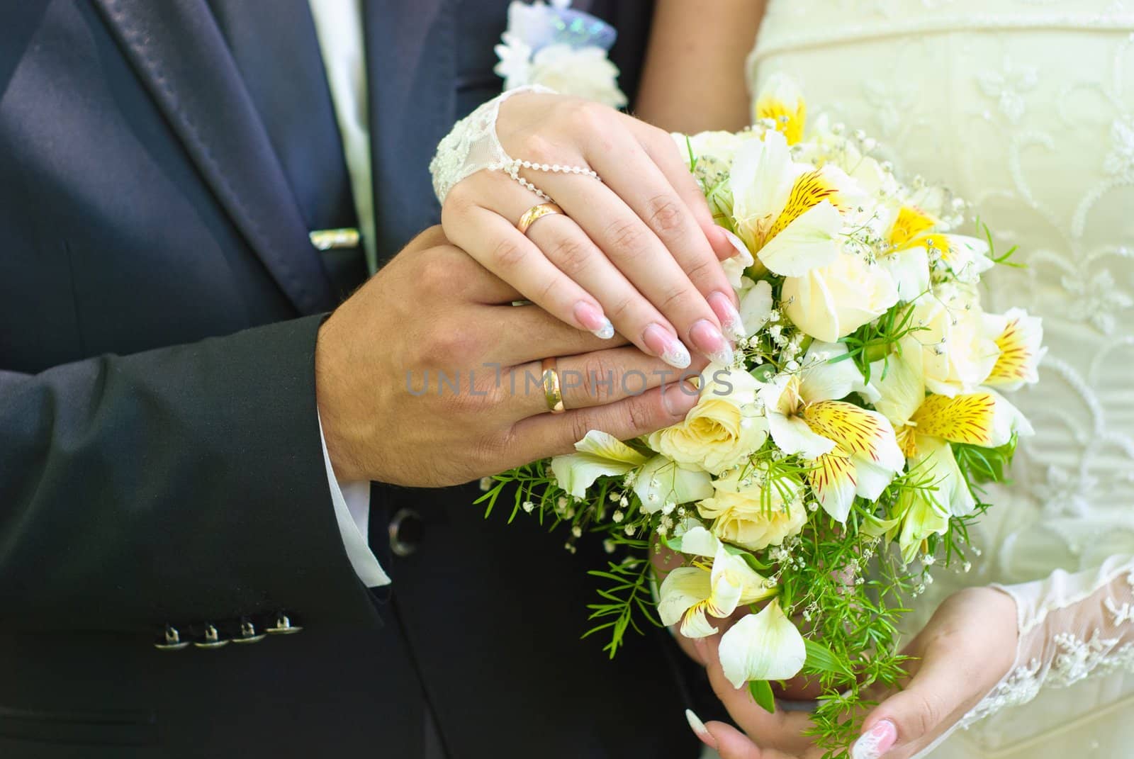 Hands of bride and groom with wedding rings over the bridal bouquet