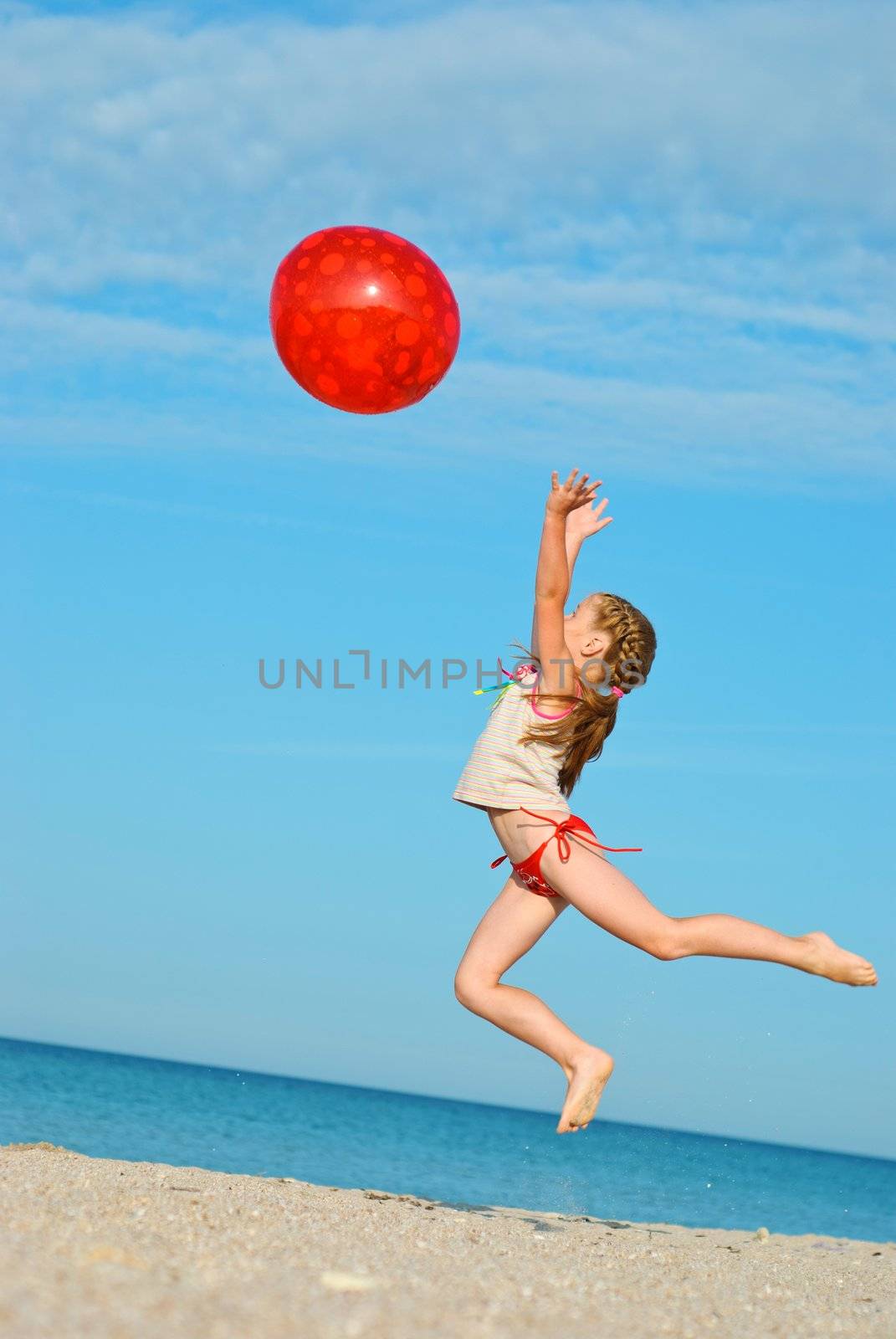 Jumping little girl with red ball on the beach