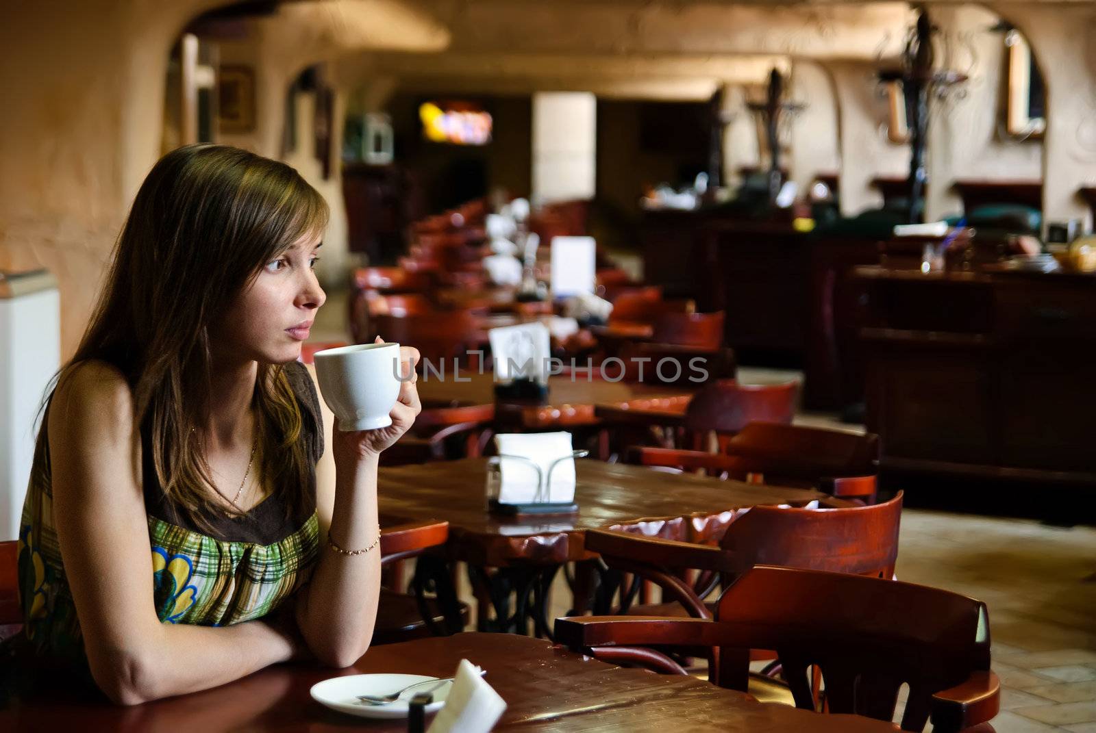 Beautiful young woman sitting in an empty cafe with a cup of coffee