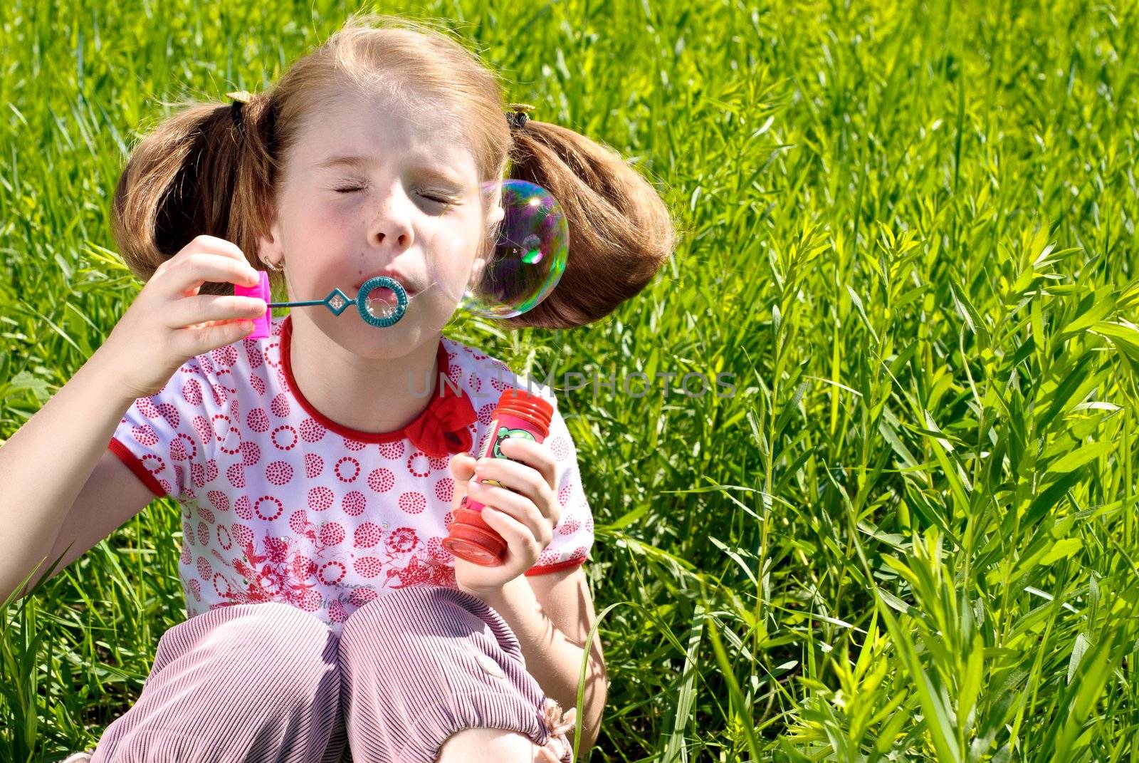 Little girl blowing bubbles on a meadow. Sunny summer day.