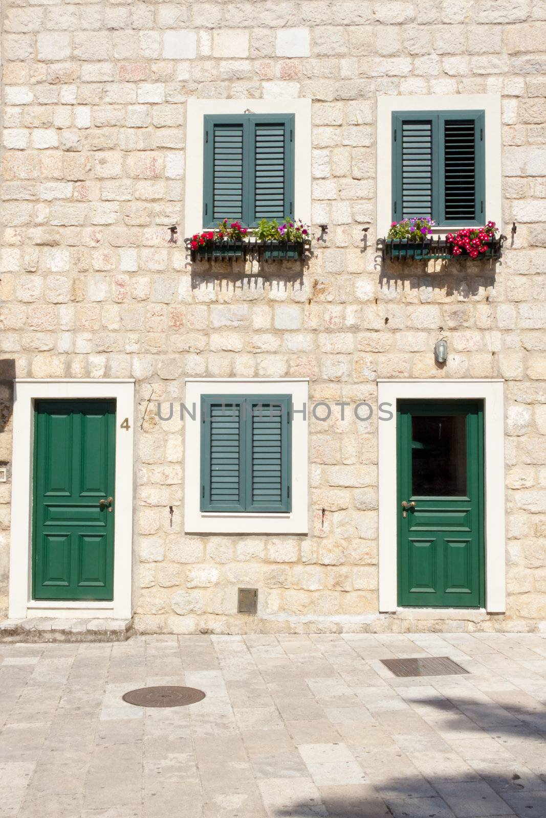 Three windows with shutters and two green wooden doors.