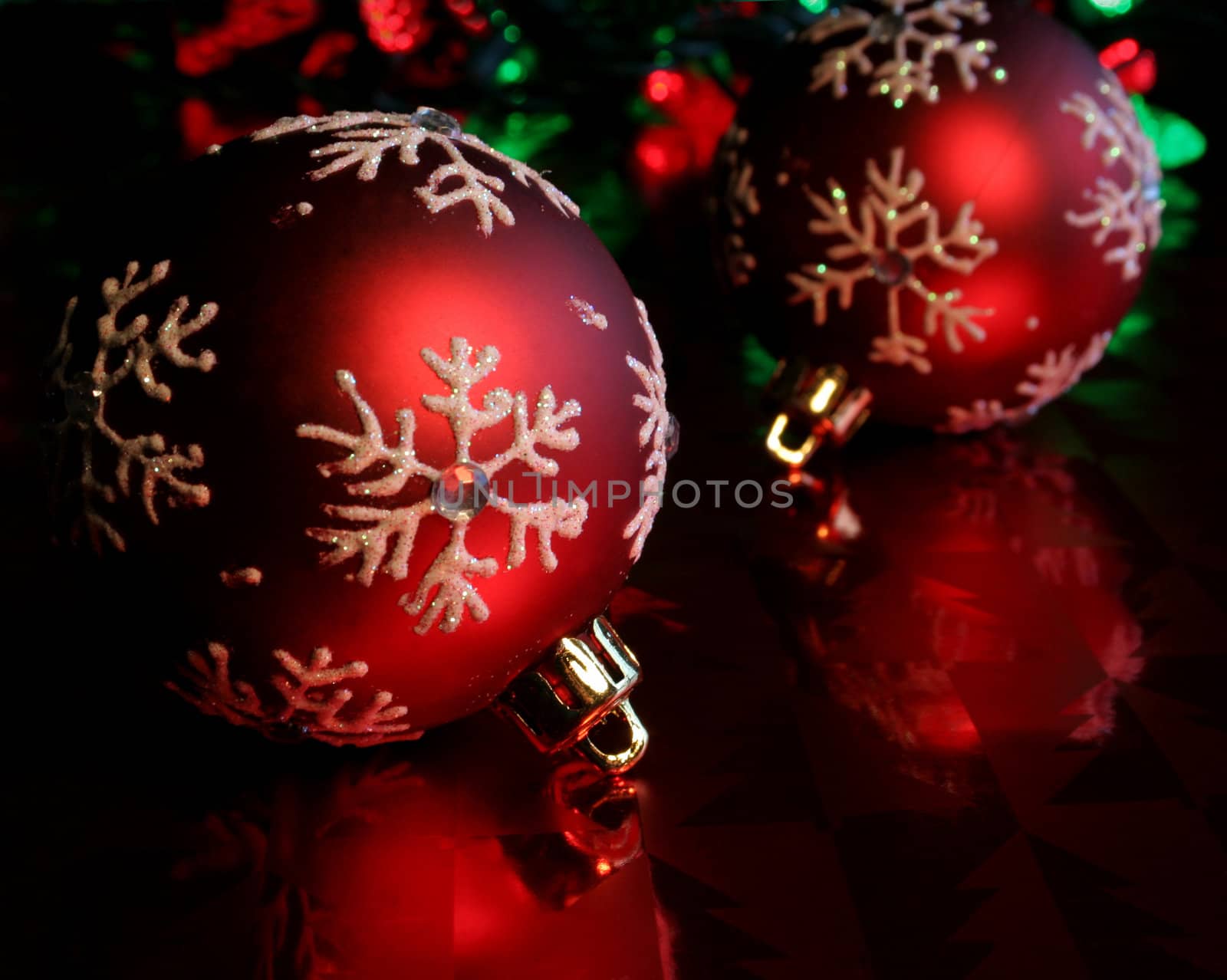 Two red christmas baubles illuminated on glossy red paper.
