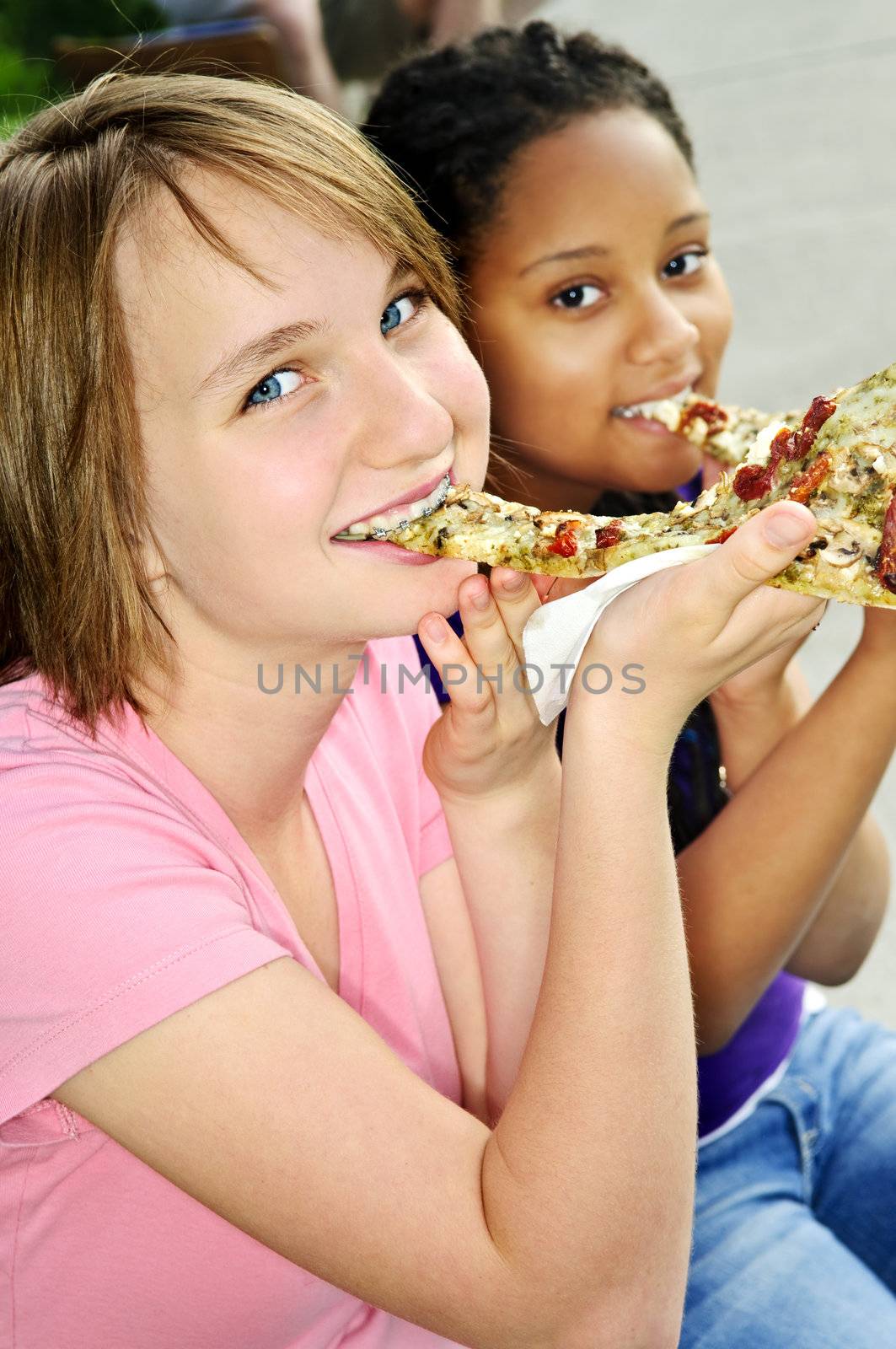 Two teenage girls sitting and eating pizza