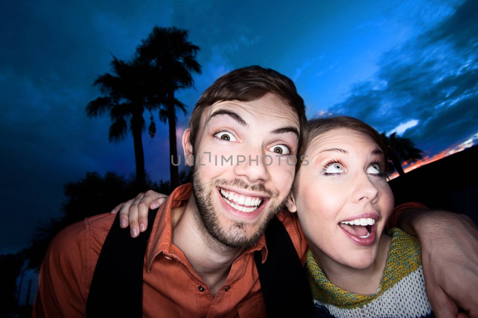 Young couple making funny faces against a blue and red sunset