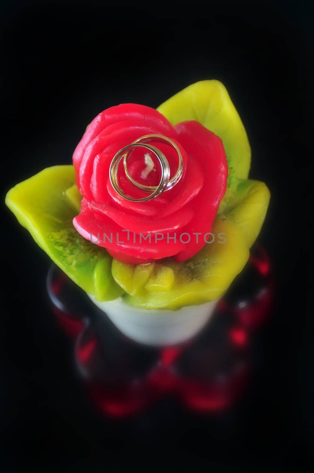 Wedding rings on red decorative candle against black background