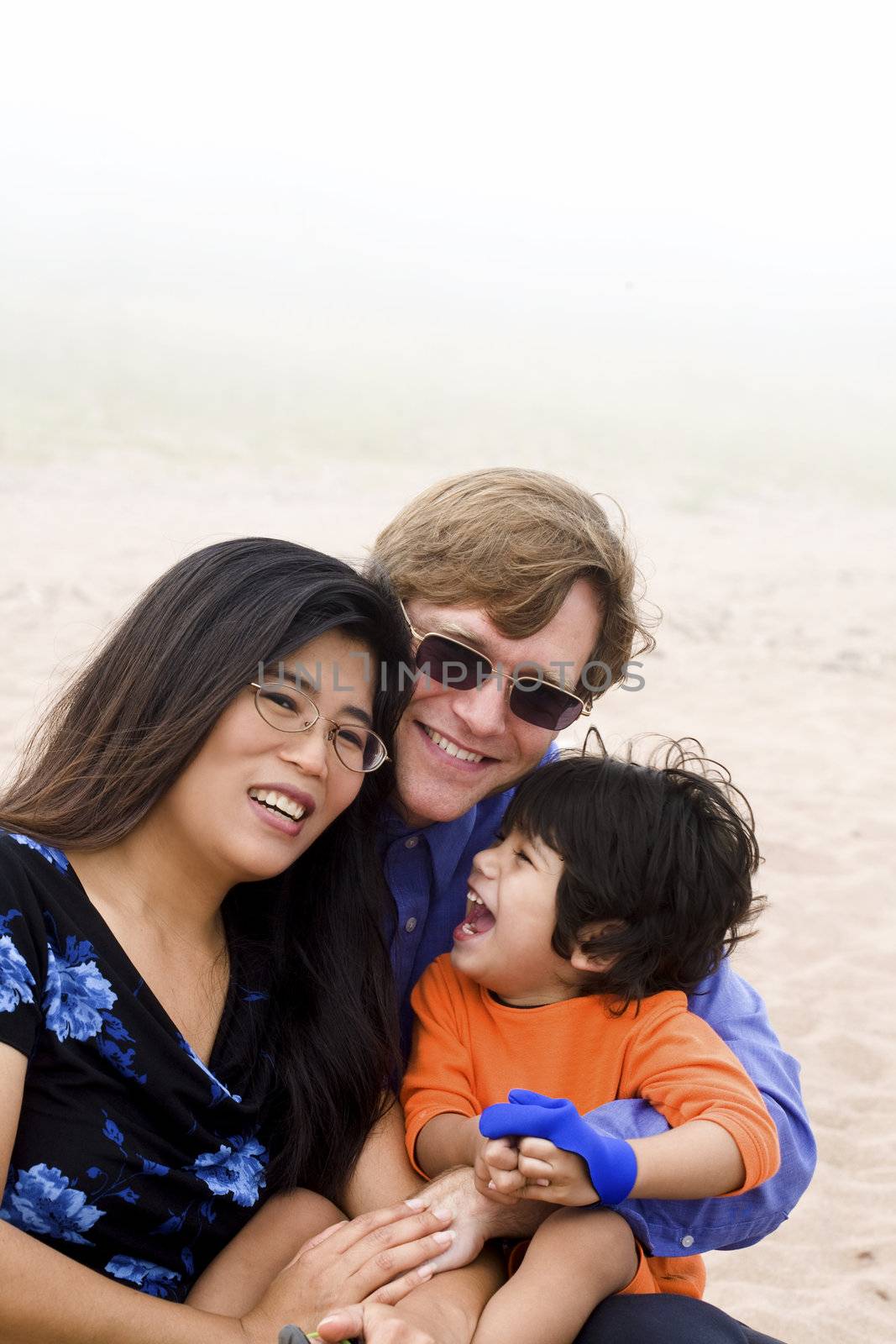 Mutiracial family sitting on beach on misty, foggy day.