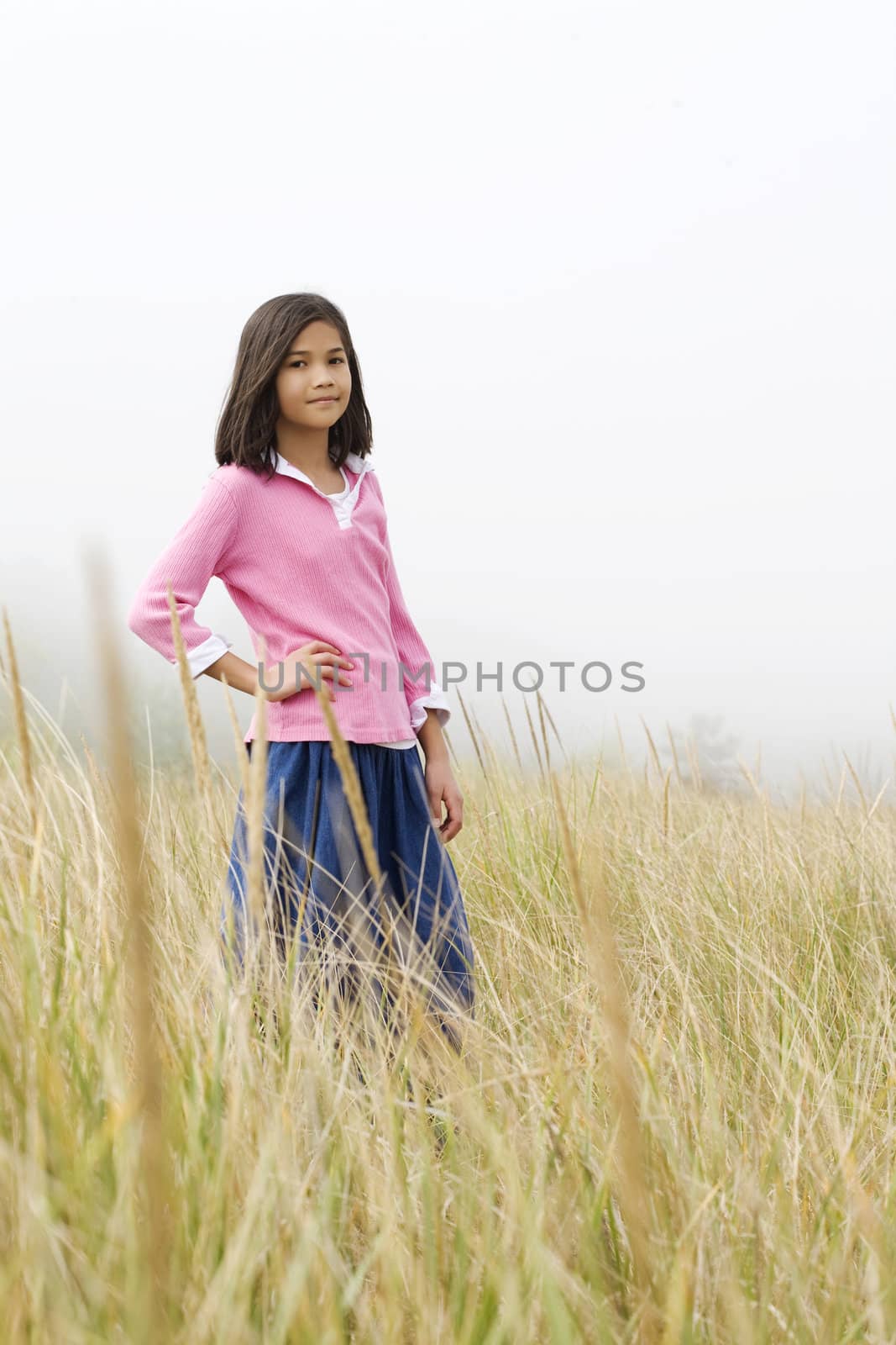 Girl standing in tall grassy field on  a misty day by beach