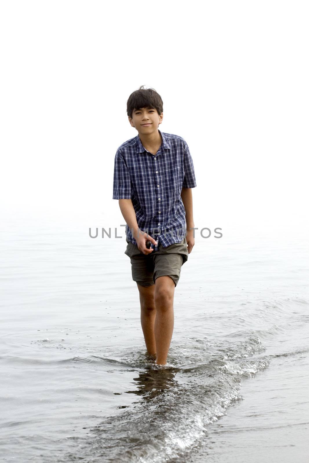 Young teen boy wading along shoreline of beach