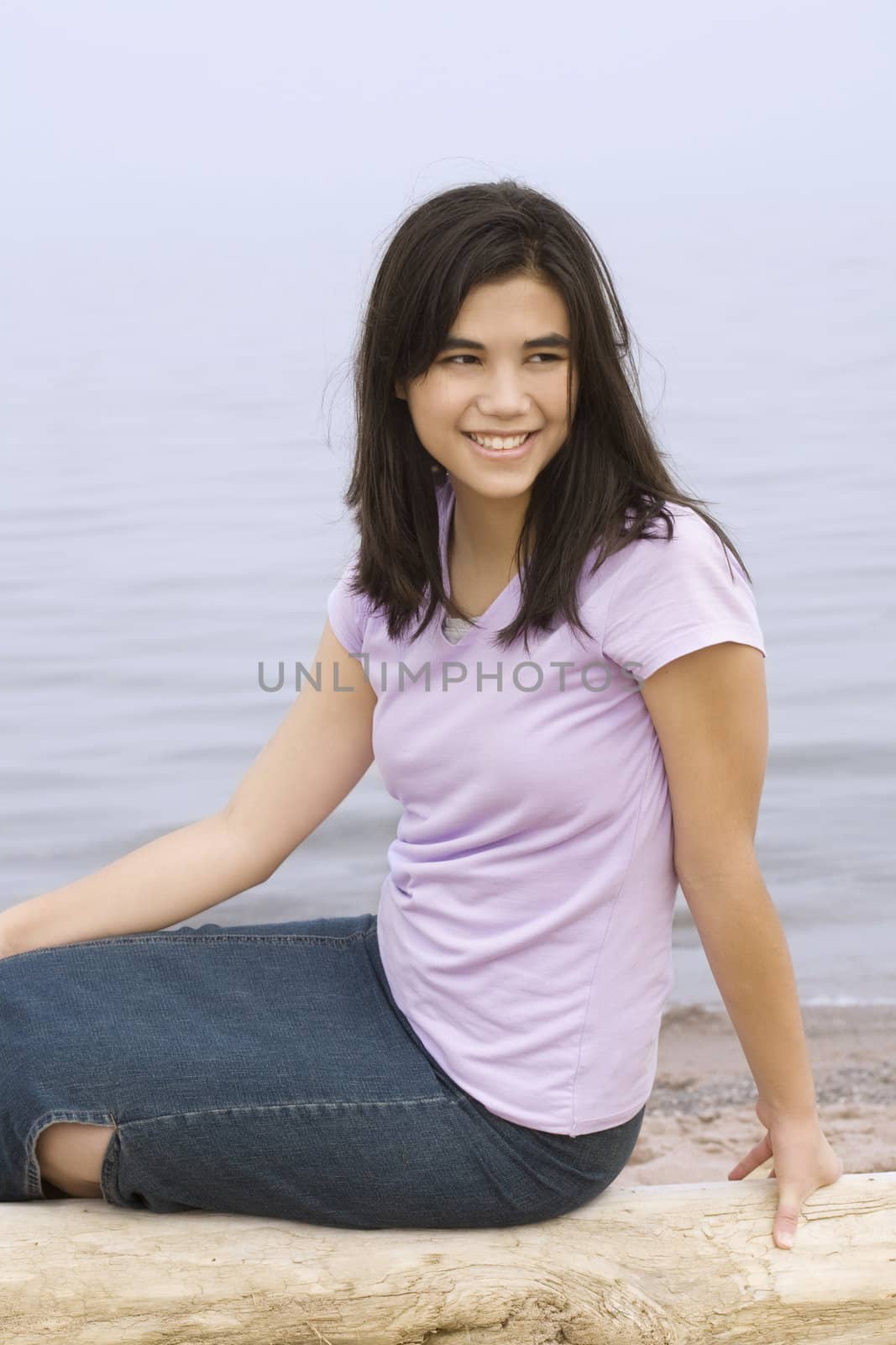 Young girl sitting on beach by lake on misty foggy day