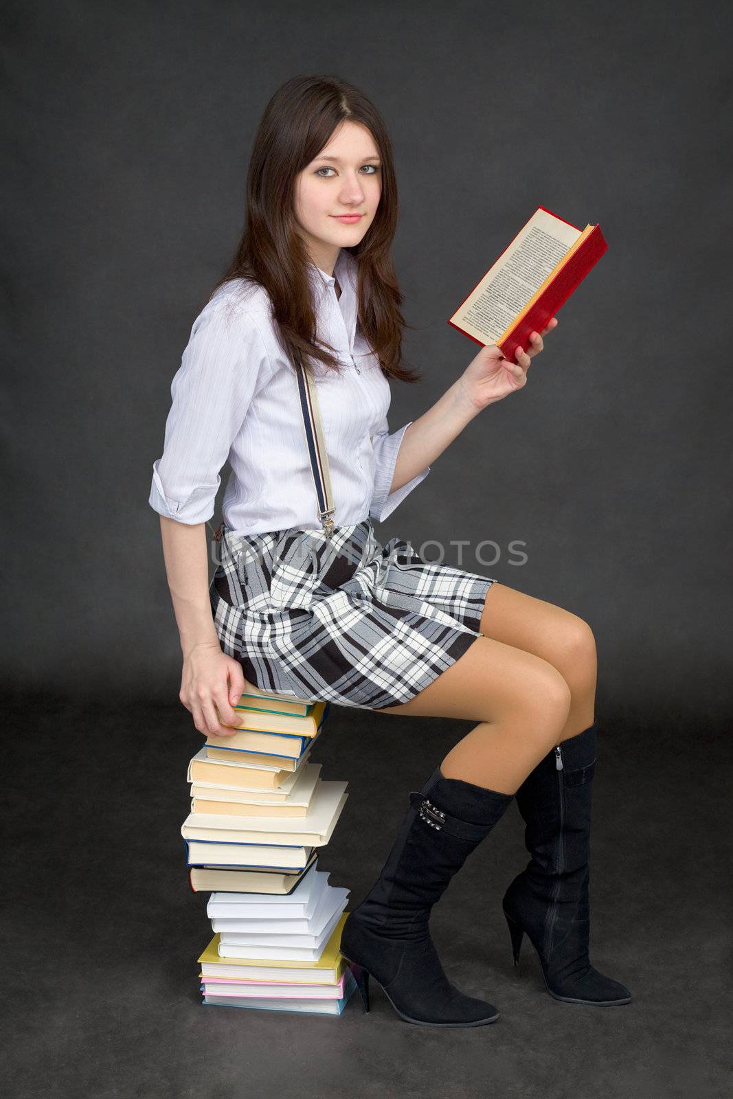 The beautiful young woman reads sitting on a pile of books on a black background