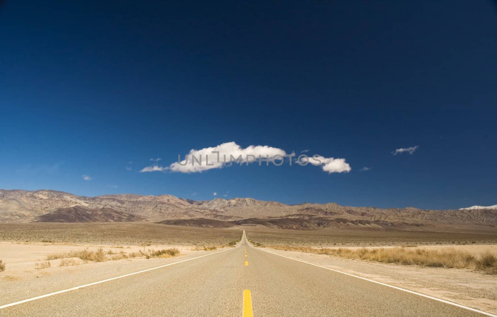 Straight road in Death valley heading into the mountains with wispy clouds overhead