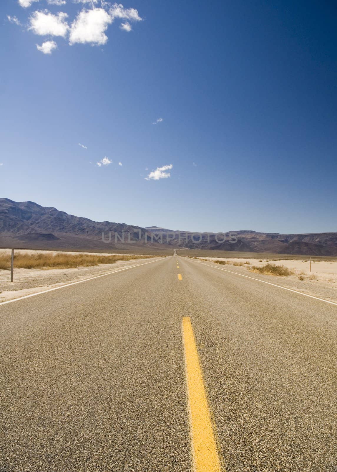 Straight road in Death valley heading into the mountains with wispy clouds overhead