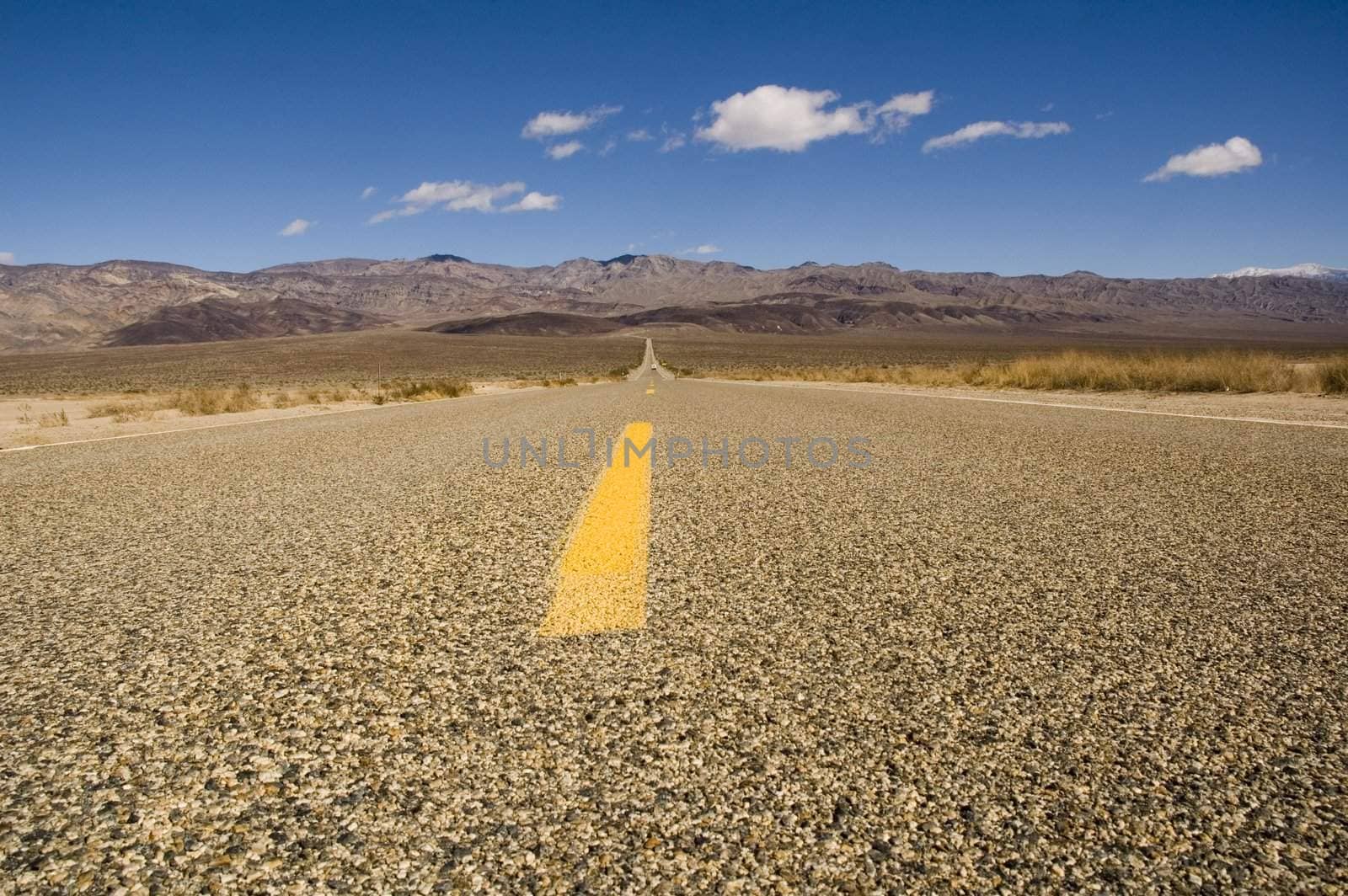 Straight road in Death valley heading into the mountains with wispy clouds overhead