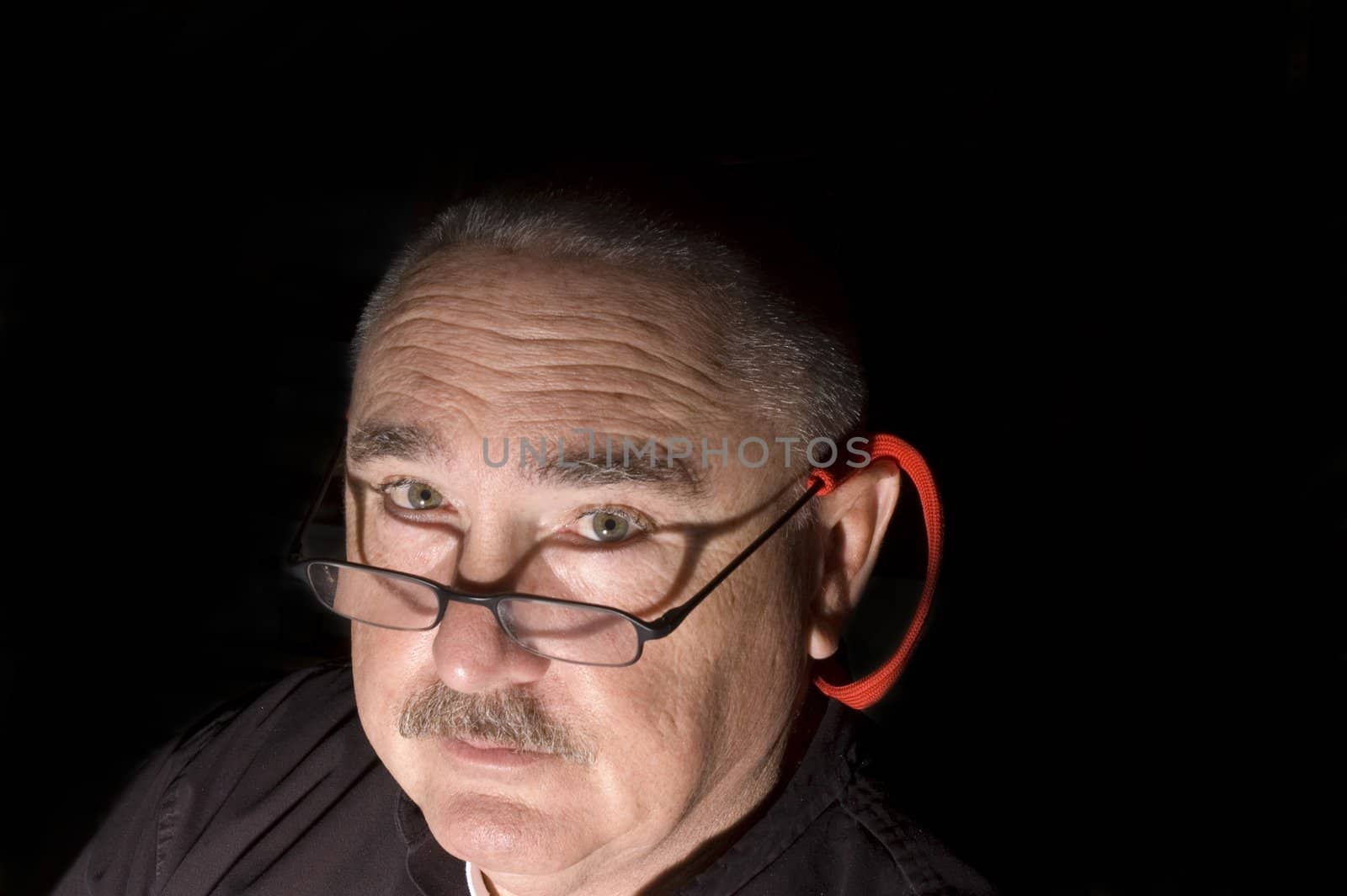 Mustached Man wearing glasses in the dark with direct light looking up