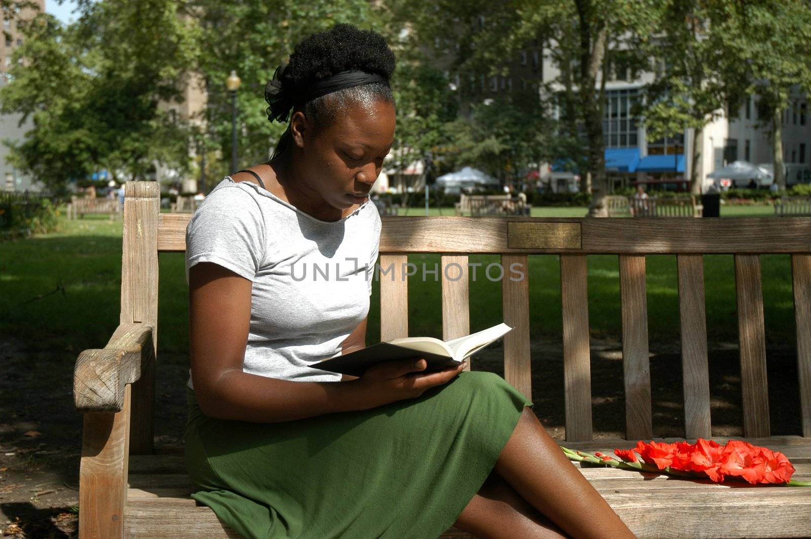 Young woman sits on a bench in a park and reads.
