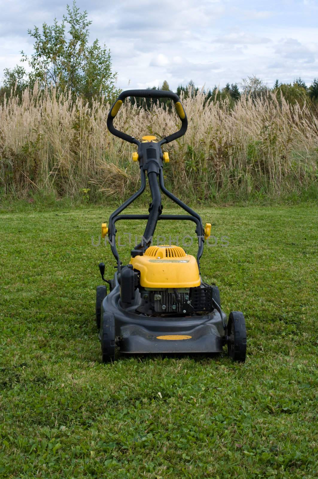 Yellow lawn mower on the green field.