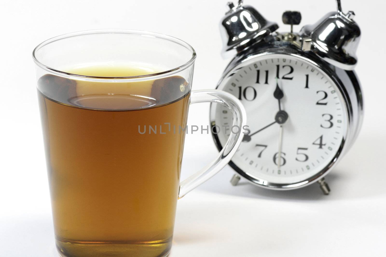 Cup of herbal tea and alarm clock over white background