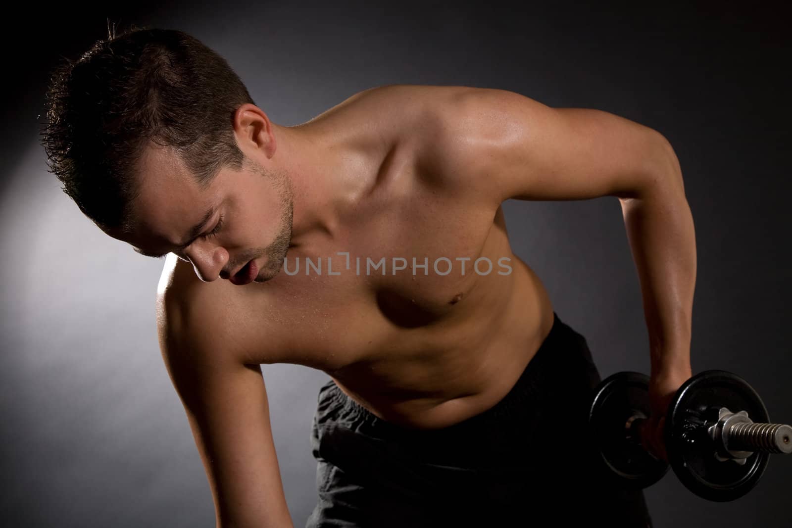 Handsome young man doing triceps exercises on black background