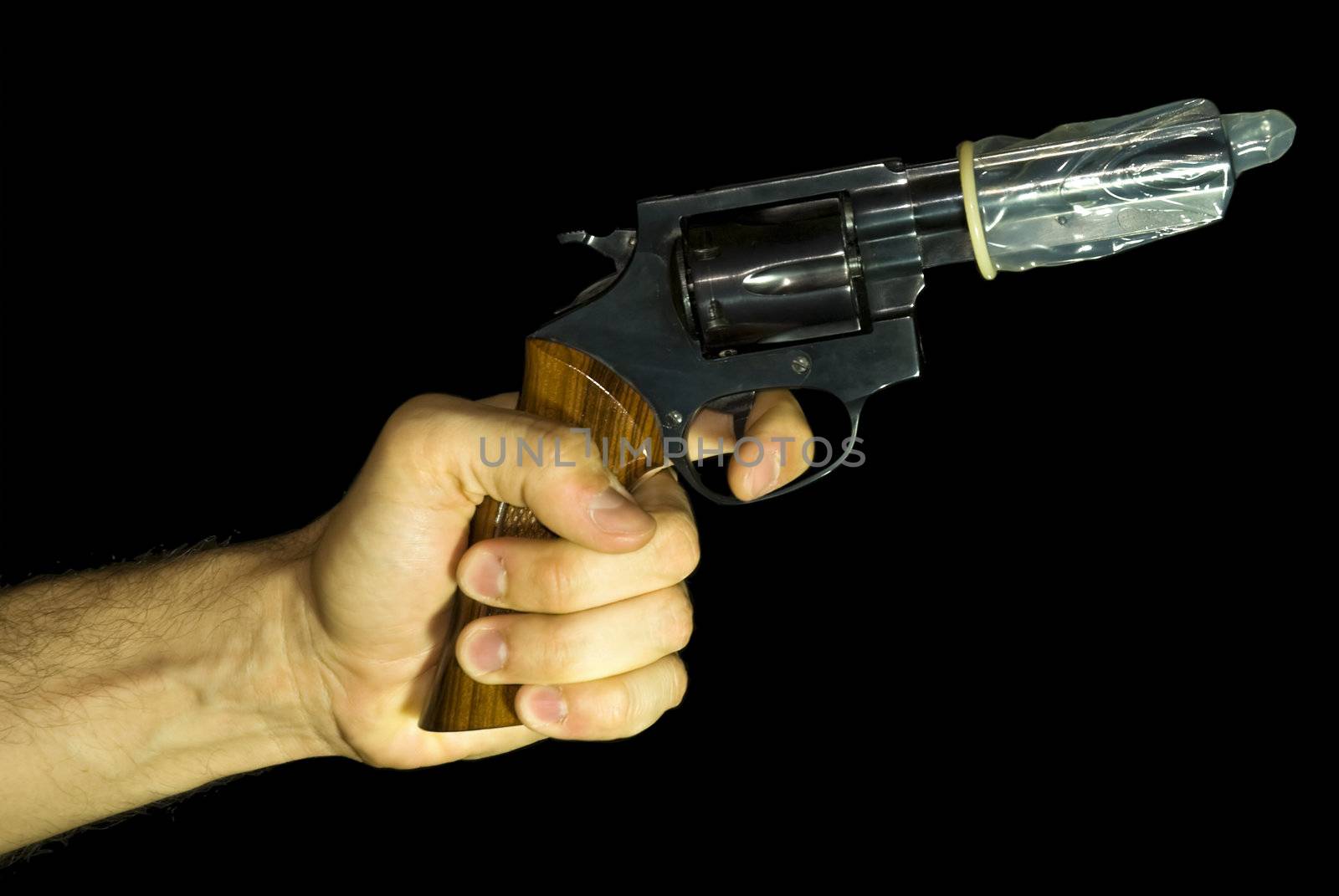 Male hand holding a revolver with a condom on it. Black background.
