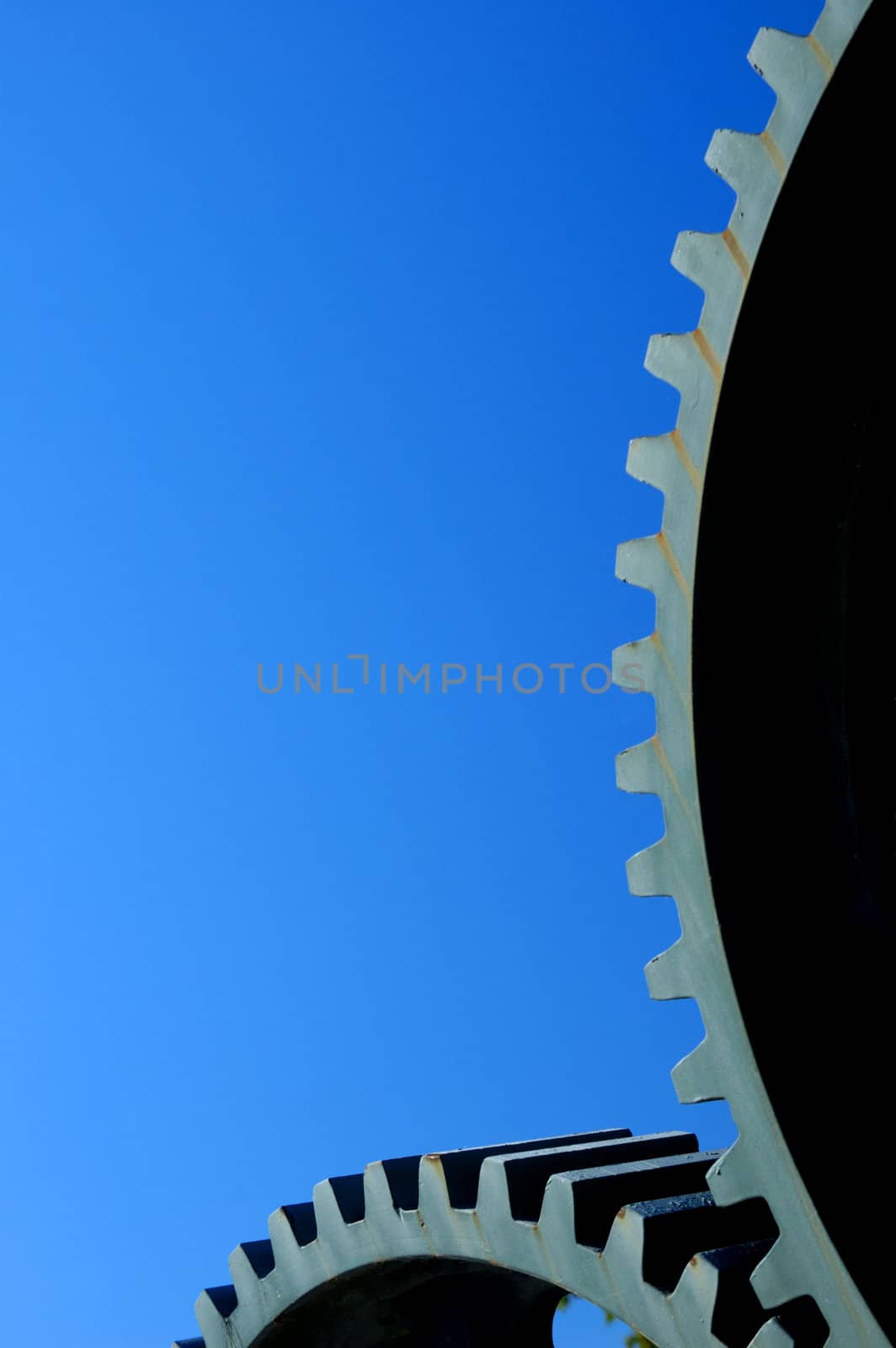 Two old interlocking gear wheels,  slightly rust-streaked, from some unidentifiable piece of machinery, set against a clear blue sky. Space for text.