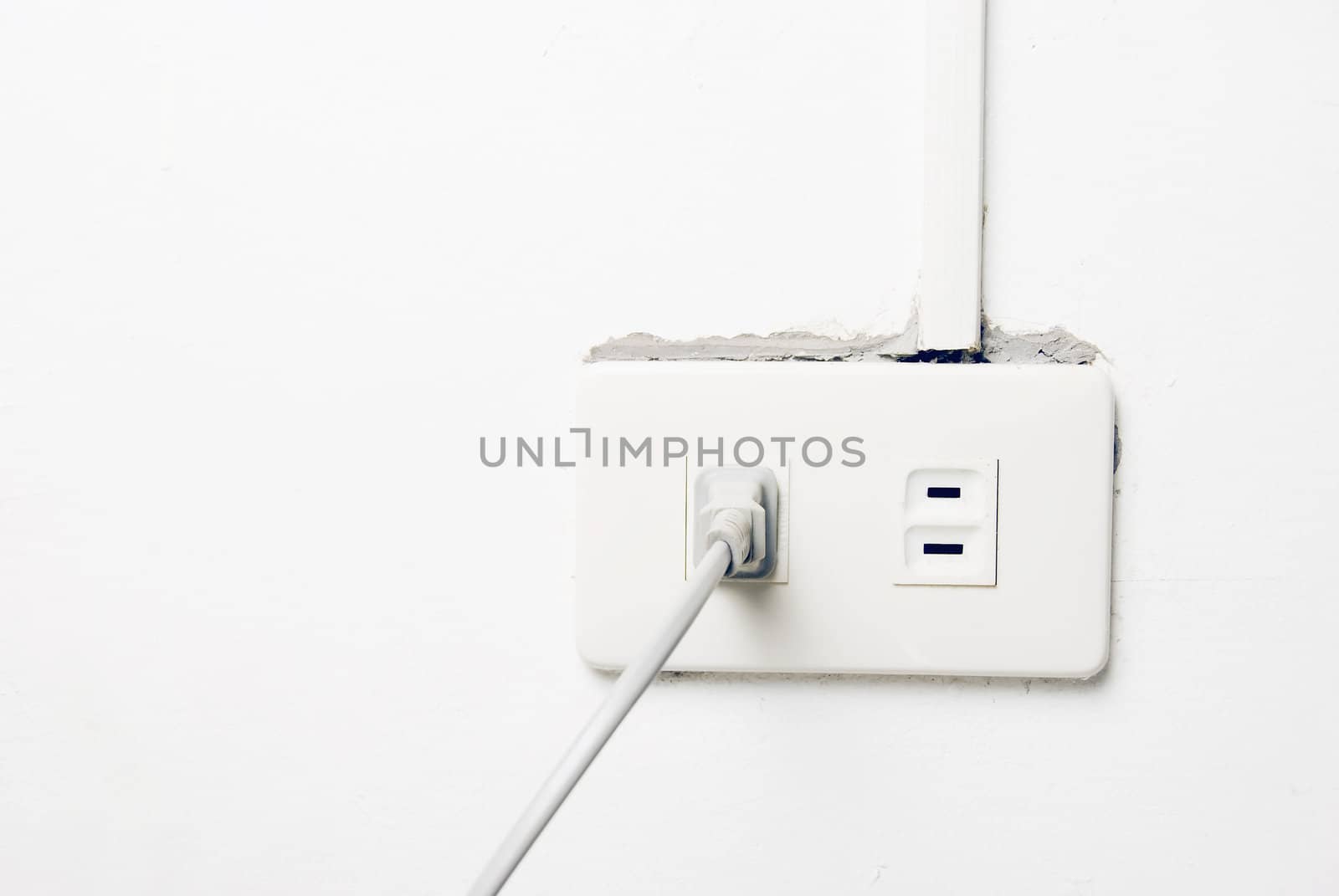 White wall socket on uneven and dirty white wall