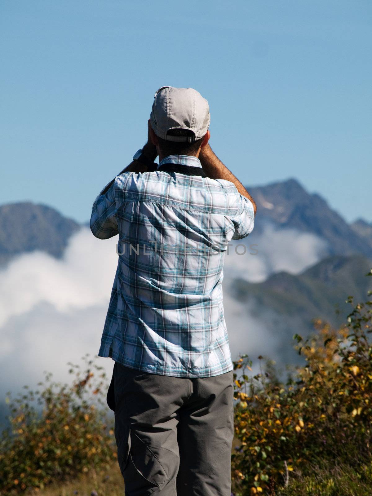 Back view of a man holding up binoculars in the mountains