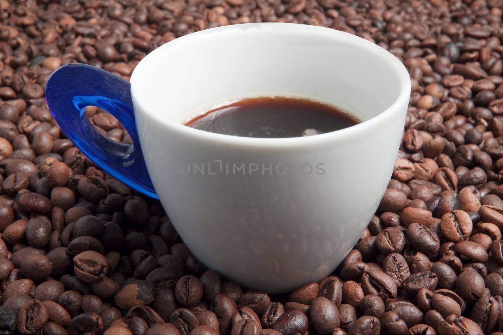 White and blue cup of coffee surrounded by coffee beans