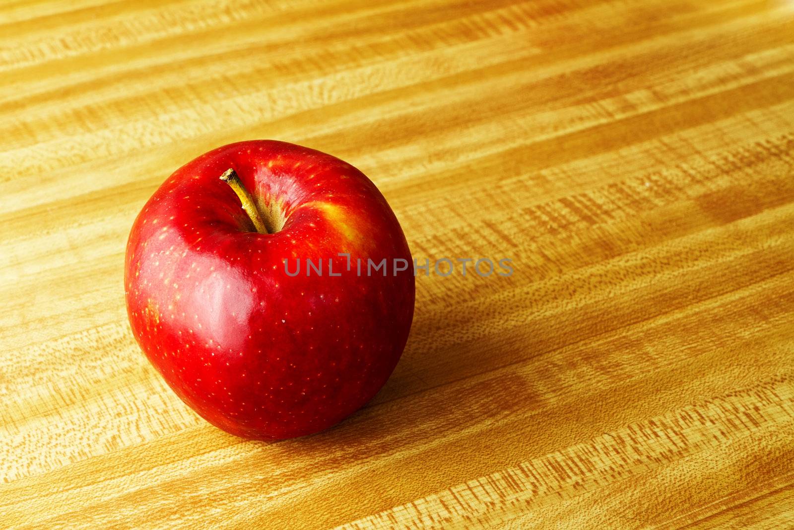 A healthy apple sitting on a wood counter top.