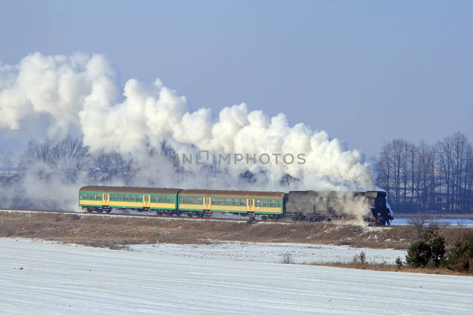 Old retro steam train passing through countryside during wintertime
