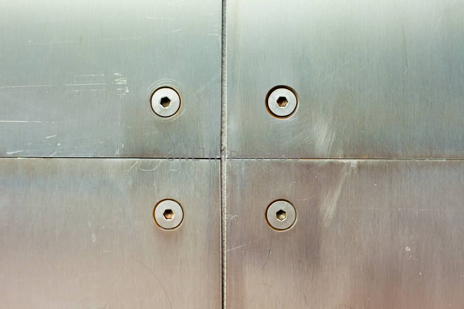Stainless steel screws holding brushed steel panel on wall of modern building.