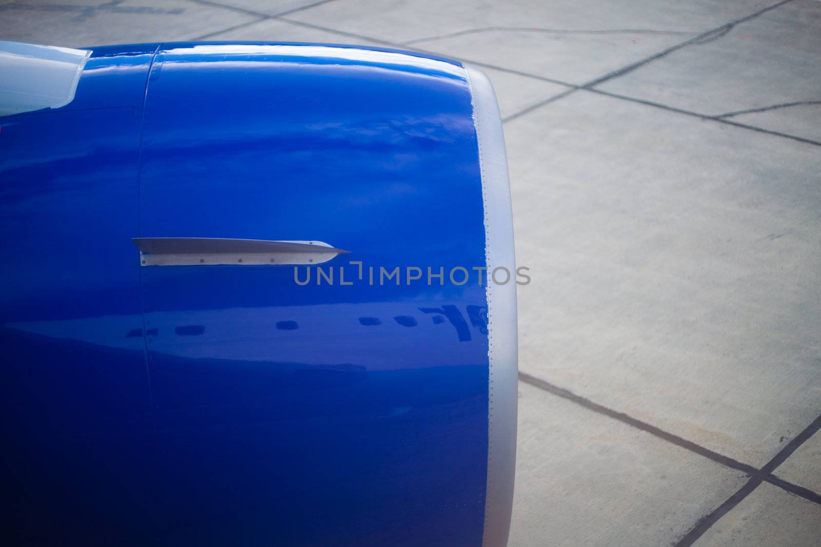 Blue metallic cover of jet engine mirroring fuselage and wing of aeroplane.
