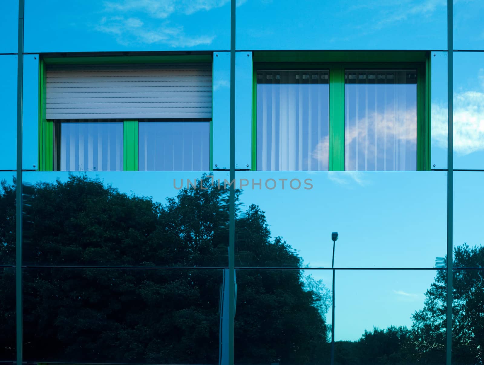 Mirrored image of environment of office building on highly reflective exterior wall with two windows.