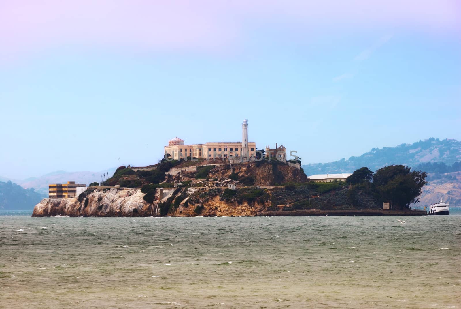 Alcatraz Island and Prison in San Francisco Bay in late afternoon with a ferry on the right side.