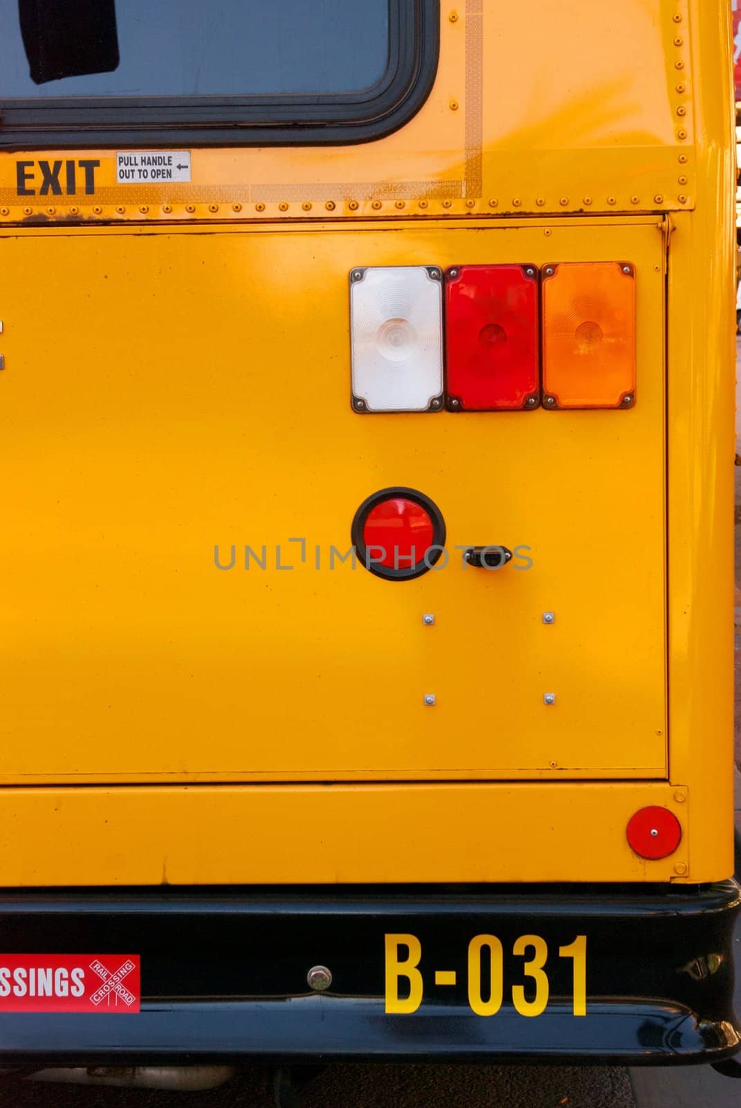 The black bumper of a bright yellow school bus with red and orange tail lights